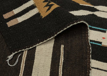 This Yei rug was woven by Navajo weavers during the second quarter of the 20th century in the Southwest United States.  The design of this rug is derived from Navajo sand painting. It features six “Yei” or holy people on a black background. The Yei alternate between orange and white and each is wearing turqoise necklaces and holds sacred eagle feathers.