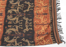 An Indonesian cotton ikat from Sumba with contrasting horizontal bands of deep indigo and warm rust. Stylized animal and ancestral motifs emerge rhythmically across the dark ground, their forms softened by the characteristic feathered edges of the resist-dye technique.
