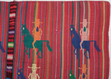 A festive Guatemalan tzute, vividly woven with striped ground in red, green, and purple tones. The textile is enlivened by repeated brocaded figures of horse and rider, depicted in bright contrasting colors of yellow, green, blue, pink, and orange each wearing a wide-brimmed hat and rendered in a bold, geometric style.