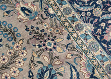 This Mashad rug was handwoven during the middle of the 20th century.

It features an allover design that radiates from a central axis with mirrored sprays of stylized palmettes, saz leaves and rosettes in shades of icy blue, indigo, shell pink and ivory on a silver ground. Nicely framed by a perfectly reconciled main border of palmettes on a midnight blue ground. The original ground color was a purple tone that was not color fast and has perfectly faded into a cool silver tone which is very uncommon in vint