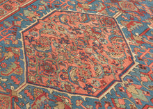 It features an atypical medallion-and-field composition centered around a coral octagonal medallion filled with angular palmettes and rosettes. The surrounding field is rendered in a softly abrashed sky-to-steel blue with scrolling vinery, serrated leaves, and stylized blossoms. The spandrels echo the motif density of the field yet shift toward coral and salmon tones that warm the overall composition. In another uncommon twist, a vertical line of single rosettes connects the spandrels, giving the piece a ba