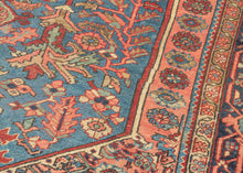 It features an atypical medallion-and-field composition centered around a coral octagonal medallion filled with angular palmettes and rosettes. The surrounding field is rendered in a softly abrashed sky-to-steel blue with scrolling vinery, serrated leaves, and stylized blossoms. The spandrels echo the motif density of the field yet shift toward coral and salmon tones that warm the overall composition. In another uncommon twist, a vertical line of single rosettes connects the spandrels, giving the piece a ba