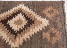 A wonderfully tactile Angora Tulu rug distinguished by its exceptionally soft, shaggy pile and striking geometric composition. Woven in a restrained palette of undyed Angora goat hair, the rug features a rich, earthy field of charcoal brown and warm taupe, punctuated by an ivory central medallion with jagged, irregular contours.