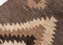 A wonderfully tactile Angora Tulu rug distinguished by its exceptionally soft, shaggy pile and striking geometric composition. Woven in a restrained palette of undyed Angora goat hair, the rug features a rich, earthy field of charcoal brown and warm taupe, punctuated by an ivory central medallion with jagged, irregular contours.