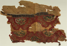 An exceptionally early Coptic textile fragment, woven more than 1,400 years ago, preserving richly patterned tapestry bands against a warm linen ground. Deep red fields are animated with scrolling vegetal forms and inset medallions containing highly stylized floral, animal, and possibly scarab-like motifs in ochre, green, cream, and dark brown.
