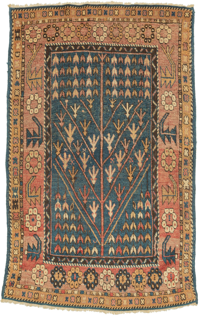 This rug was by Kurds during the first quarter of the 20th century.  It features an abstracted and directional tree of life motif on a cerulean ground. Framed by a main border that alternated between rosettes and serrated leaves on the sides but is composed solely of rosettes on the top and bottom. 