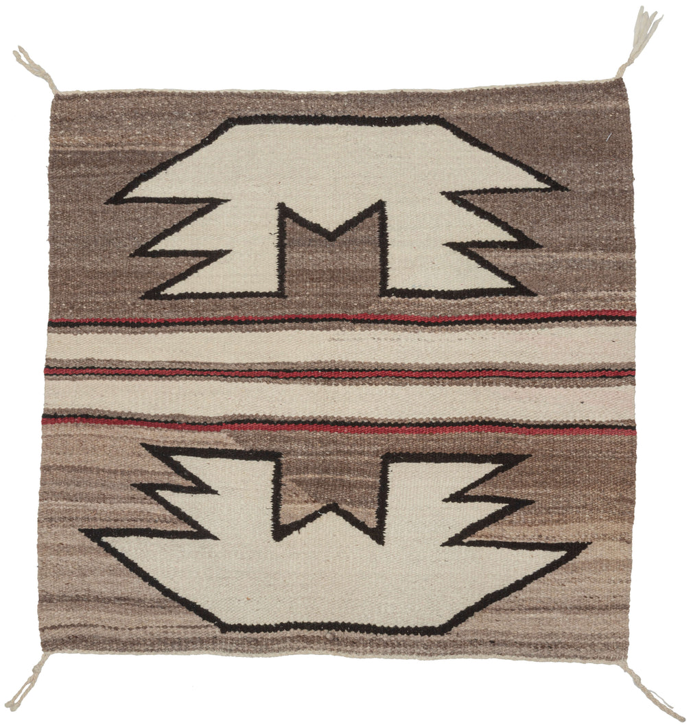 This&nbsp;Navajo rug was handwoven in the southwest United States during the 2nd quarter of the 20th century.

A beautifully balanced small-format Navajo weaving, showcasing bold symmetrical motifs rendered in a ground of hand-spun, natural wool tones. Graphic stepped&nbsp;forms float against soft variegated browns, mirror one another on each side of a classic banded center that is accentuated by&nbsp;warm red accents.