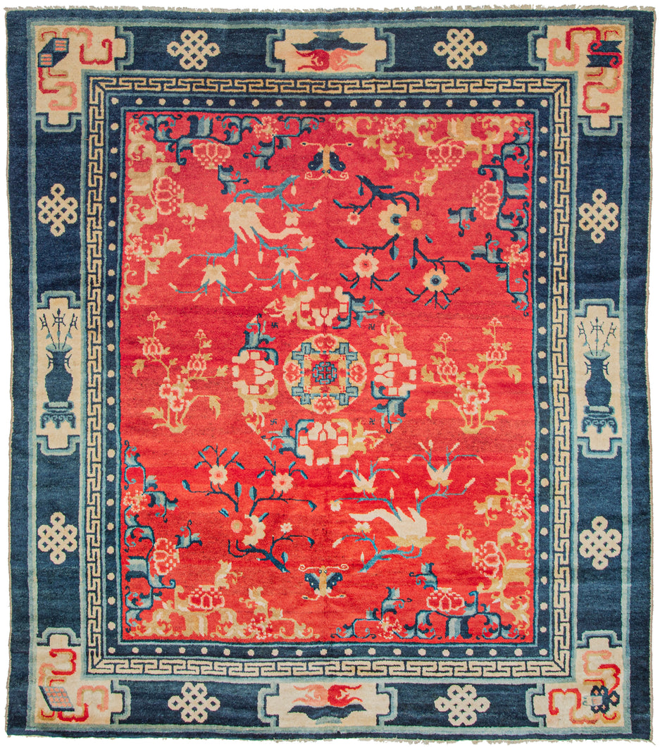 The main design is composed of a central mandala, encircled by flower branches and blossoms on a rich red ground. This red tone is very auspicious and often associated with prosperity. The main border design separated into cartouches that include and various auspicious symbols. Between each cartouche is an endless knot symbol. The minor borders feature the classic pearl motif and greek key motif.