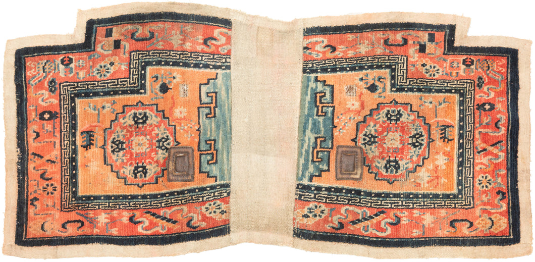 This saddle blanket was woven in Tibet at the turn of the 20th century.  This rugs are known as a Makden and were intended to be used under a horse saddle in Tibet. This piece has been woven in two pieces and attached with cotton fabric. Two leather pieces have been woven in to attach the blanket to the animal. Each half features a mandala filled with four bats on an orange ground and a lively blue cloud motif where the halves interface.. The outer border features cloud-bands and auspicious symbols.