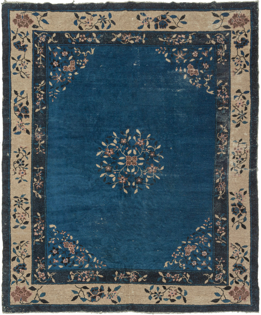 Features a central medallion and four cornices of blossoming flowers on an open and expansive blue field. Framed by nicely spaced main border of individual flowering branches of an ivory ground and finished with a solid block of navy around the perimeter. Peking rugs were created for the British market and the palette was utilized to emulate the look of blue and white Chinese porcelain which was extremely popular in the West.