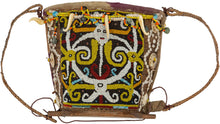 A richly adorned Dayak baby carrier from Borneo, made with a wooden frame, woven fiber body, resist-dyed cloth lining, and a densely beaded front panel. The design is worked in glass beads with bold yellow, white, black, red, and blue motifs, likely representing protective ancestral or spirit forms.

Among Dayak peoples, baby carriers were both practical and symbolic. Worn on the back, they held the child securely while also serving as objects of protection, status, and family care. Beadwork, shells, bone o
