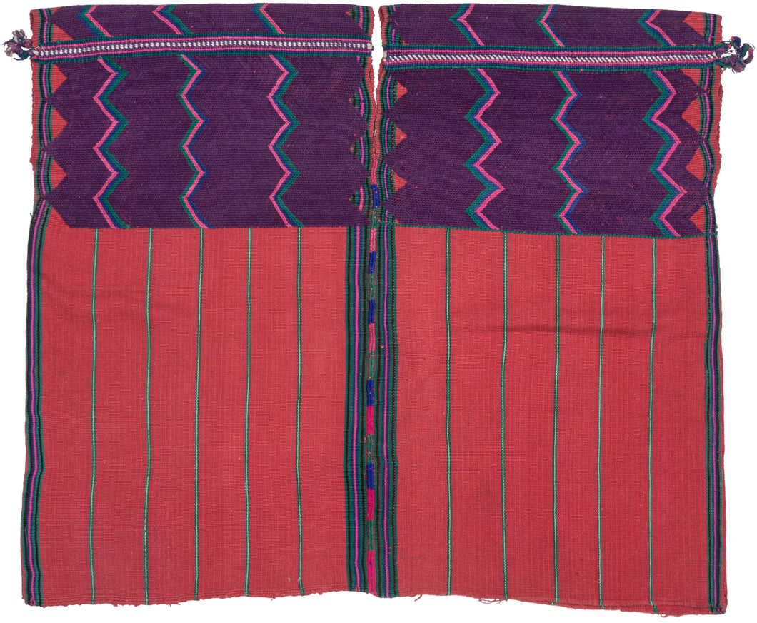 A bold highland huipil woven with striking contrast of deep purple and brick red. The upper section is patterned with vivid zig-zags in pink, green, and turquoise, while the lower body panels feature a calmer striped red ground. Woven on a backstrap loom, this piece balances geometric energy with grounding simplicity, making it both a traditional garment and a statement textile.