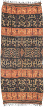 An Indonesian cotton ikat from Sumba with contrasting horizontal bands of deep indigo and warm rust. Stylized animal and ancestral motifs emerge rhythmically across the dark ground, their forms softened by the characteristic feathered edges of the resist-dye technique.