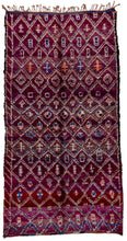 This Marmoucha rug was woven in the Middle Atlas mountains during the 20th century.  It features a diamond lattice design in orange, ivory and blue on a purple ground. Various purples are present shifting from wine to grape soda. The lattice is filled with simple shapes and protection symbols. There is a partial border only to one side. 