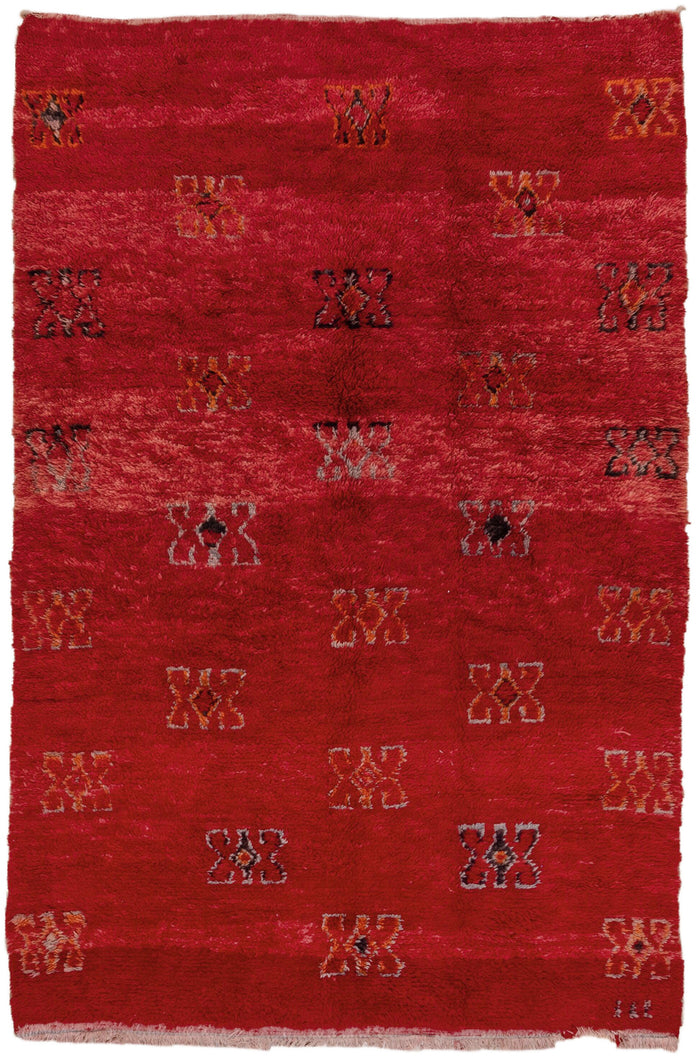 This Moroccan rug was woven in the Middle Atlas mountains during the 20th century.  It features a powerful variegated red ground full of large butterfly-esque protection symbols in black, orange and purple. 