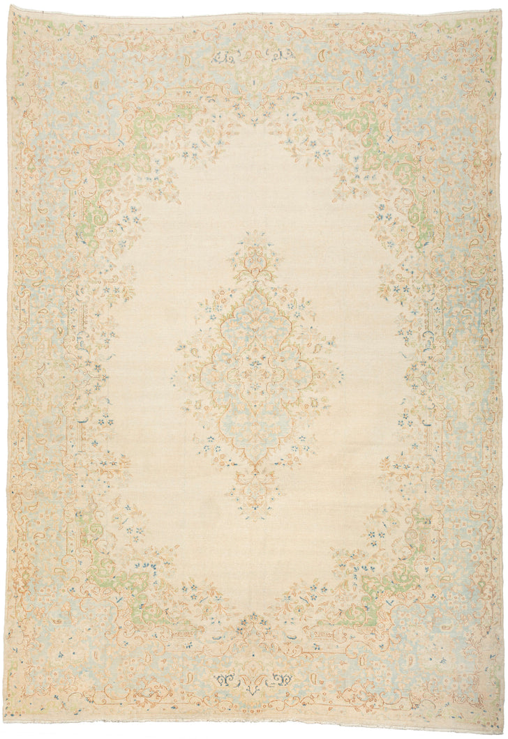 This Kerman rug handwoven during the middle of the 20th century.   It features an ornate central medallion of muted floral sprays in powder blue, indigo and green on a creamy ivory ground. It is framed by a grand baroque style border. A soft and elegant piece that will subtly elevate any space.