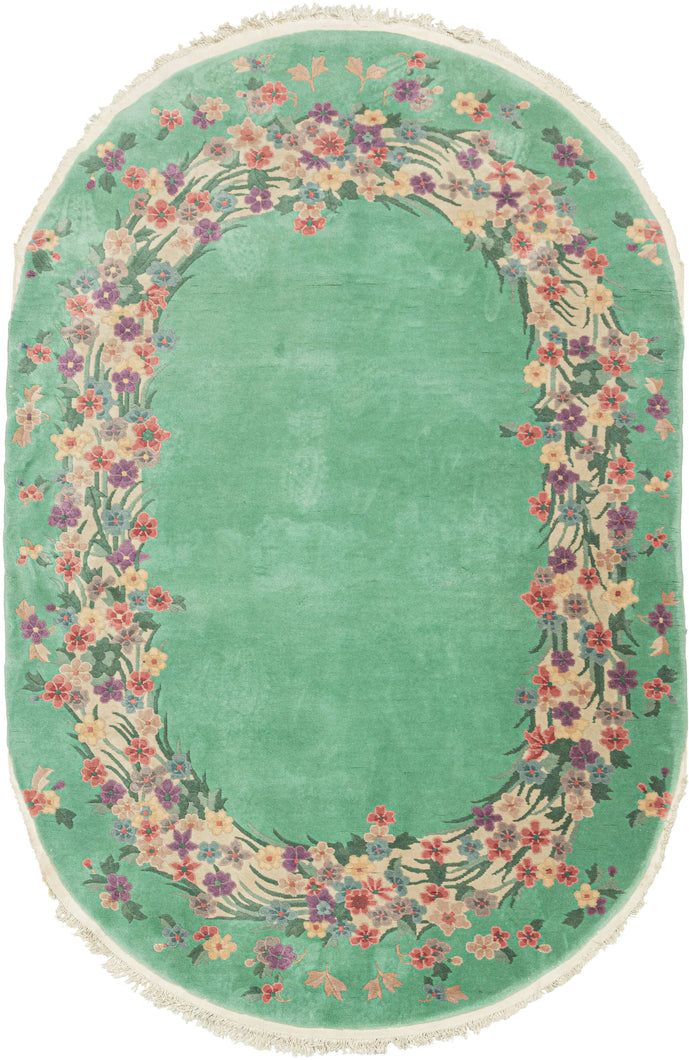 This Oval Chinese Deco Rug features an open field of seafoam green. Its unadorned center is surrounded by an oval ring of various multicolored blossoms. Single rosettes adorn the outer perimeter of the oval ring.  In very good condition, with full even pile. Pile is thickly woven and medium height, with a sturdy handle. 