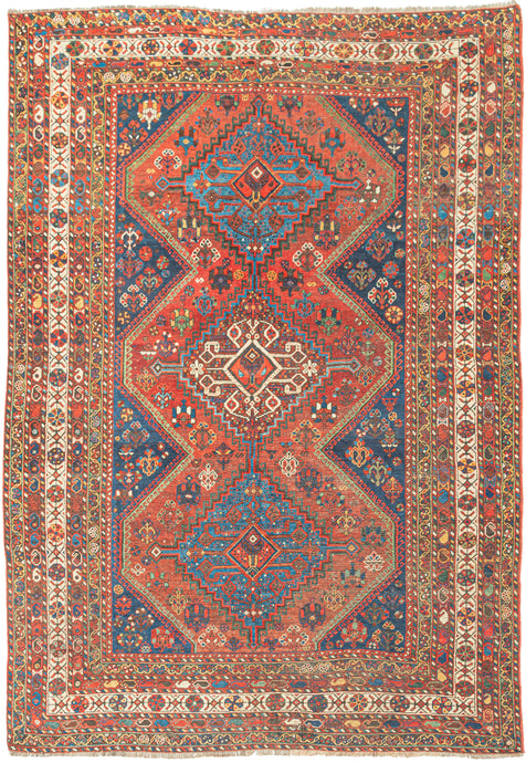 This Khamseh rug was handwoven during the second quarter of the 20th century. It features a field of three connected latch-hooked medallions and various rosettes and flowering shrubs floral motifs. Rendered in a vibrant jewel tones of blue, green, red and yellow with ivory and brown accents. An energetic ivory main border is flanked by minor borders of polychrome botehs that sparkle like rows of Christmas lights.