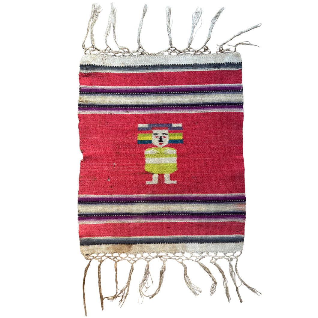A small Zapotec weaving from Oaxaca, Mexico, likely mid–20th century, featuring a boldly stylized dancing figure at center. Rendered with outstretched arms and parted legs, the figure suggests festive movement. It wears a lime-green costume and balances a rainbow-striped headdress, evoking the colorful attire of Oaxacan fiestas and traditional dance ceremonies The figure is framed by a saturated red ground and bordered with narrow horizontal stripes in purple, white, and black. Braided wool fringe finishes 