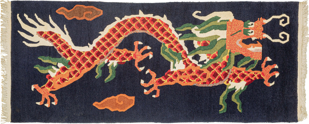 Tibetan carved rug It features a four clawed dragon flying through the clouds. In red, orange and yellow scales with ivory, light and dark green accents that pop against an open navy ground. The claws and face are rendered in red and yellow static and details like the dragon's scales and mane have been hand-carved with a razor adding extra detail and interest