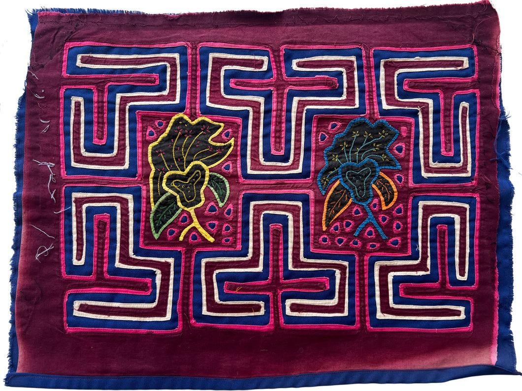 Vintage Mola cloth handmade by the Guna (previously spelled Kuna) people of the San Blas Islands.  Mola is a reverse appliqué technique, similar to the technique used in quilting but using multiple layers of different-colored cloth that are first sewn together before a design is created by cutting away different layers. These cloths are traditionally made in pairs to be worn on the front and back of women's blouses.  This Mola features two central floral forms surrounded by a maze like motif.