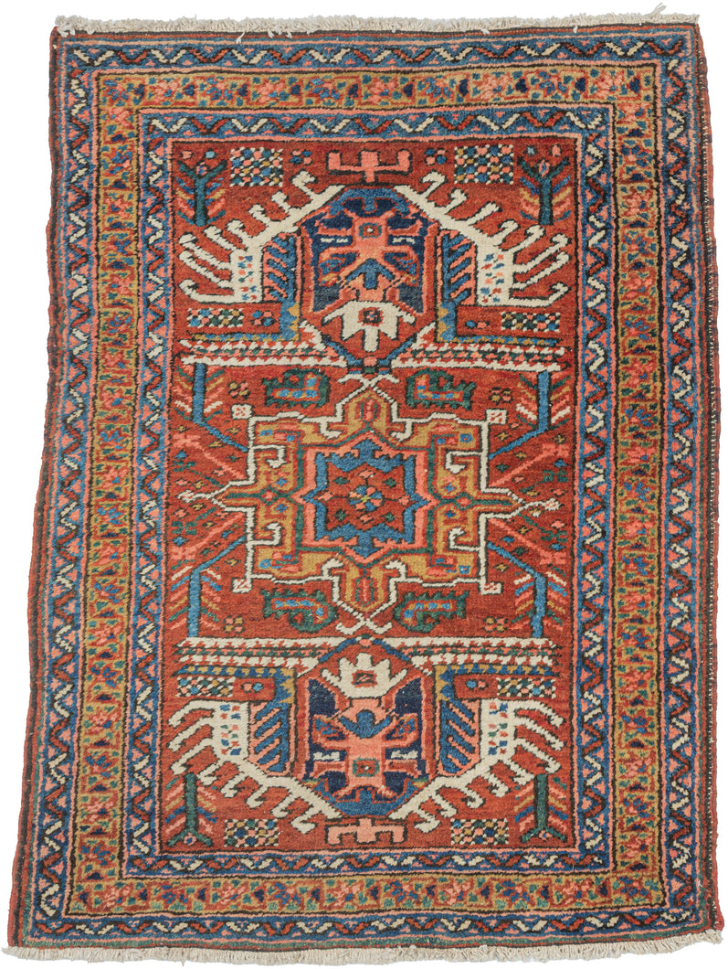 A bold small rug woven in the Heriz region using a classic Karaja design vocabulary. The saturated brick-red field is organized around angular medallion forms and animated geometric motifs with a lively, almost architectural energy. Crisp cobalt blue and ivory accents create strong contrast, while the finely drawn borders frame the field with rhythm and balance.