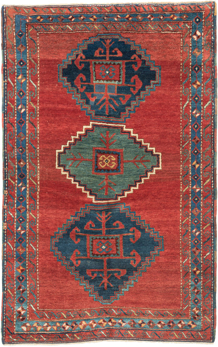 This Kazak rug was handwoven in the Southwest Caucasus during the early 20th century.

A striking example featuring three boldly drawn stepped medallions set against a vibrant, glowing red field. The palette is classic Southwest Caucasian: deep indigo, moss green, ivory, and saturated natural reds that radiate warmth and energy. The central medallion really pops and is distinguished by a lovely jewel toned blue green and enhanced by a starkly contrasting ivory outline that giving the piece strong graphic pr