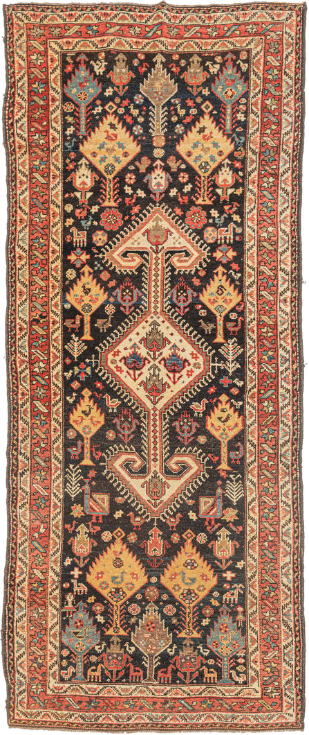 This stunning rug features a vertical medallion design on a deep indigo blue field. The field is filled with a fantastical world of various trees and plant forms surrounded by all types of animals. There are multiples types of birds including peacocks as well as two human figures near the bottom of the composition. The world is wonderfully painted with contrasting tones of reds, yellow, ivory, and aubergine. Lori rug