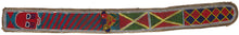 A striking Yoruba beaded sash from Nigeria, densely worked with glass beads in bold red, blue, green, yellow, white, and black. The long narrow form is divided into geometric panels with diagonal bands, diamond motifs, and a dramatic raised mask-like face at one end.