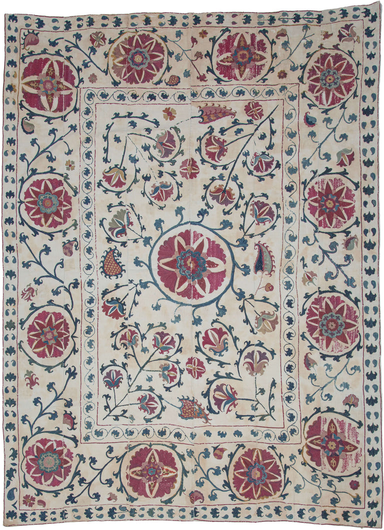 A finely embroidered Nurata suzani featuring a central floral medallion surrounded by scrolling vines, blossoms, and stylized pomegranates. The field is framed by a border of large circular rosettes that echo the central motif and create a balanced architectural composition.
