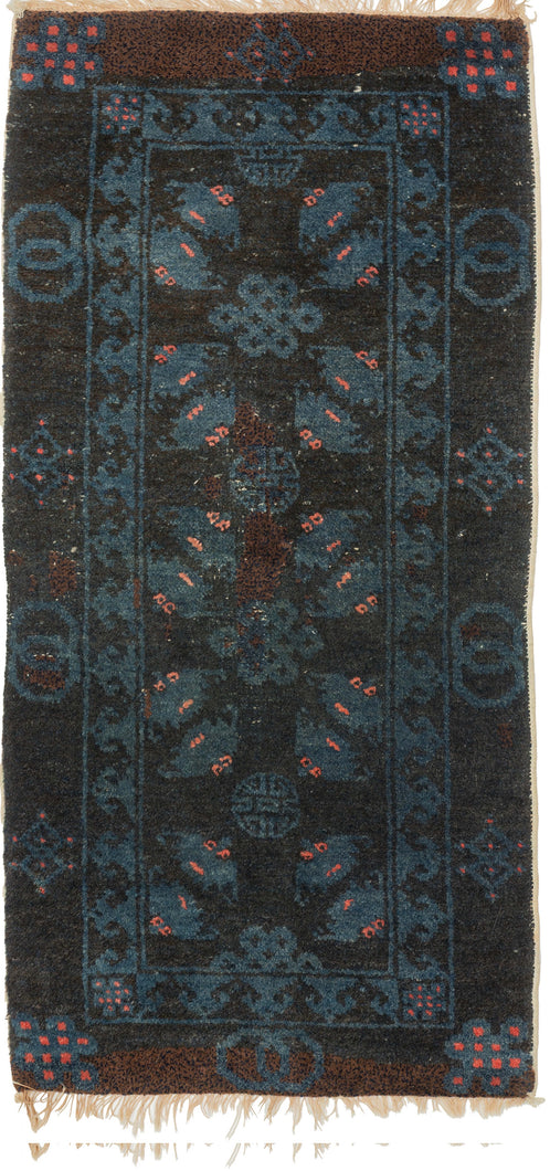A small Gansu rug woven with a lively arrangement of auspicious symbols against a deep navy field, accented in indigo blue, coral, and muted aubergine. Pairs of stylized bats appear throughout the central field, arranged around endless knots and&nbsp;shou symbols, while interlocking ring motifs line the outer border.

In Chinese decorative arts, the bat is a symbol of good fortune, while the shou character represents longevity and the endless knot suggests continuity and enduring harmony. Together
