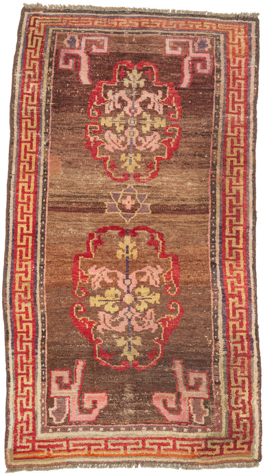 A character-rich Tibetan rug with a warm brown field and bold medallion motifs framed by a striking red key border. The saturated reds and soft pinks contrast beautifully against the earthy ground, while subtle abrash and wear create depth and texture across the surface.