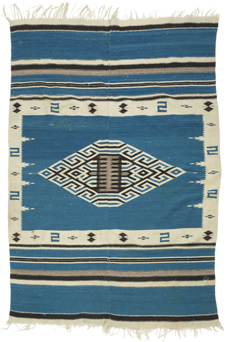 This serape was handwoven in central Mexico during the middle of the 20th century.

A luminous Texcoco serape distinguished by its saturated indigo field and a well articulated central diamond medallion. The stepped, labyrinthine geometry—woven in crisp natural white and deep black creates a powerful visual anchor, while the serrated motifs and butterfly-like accents along the border add nice rhythmic movement.