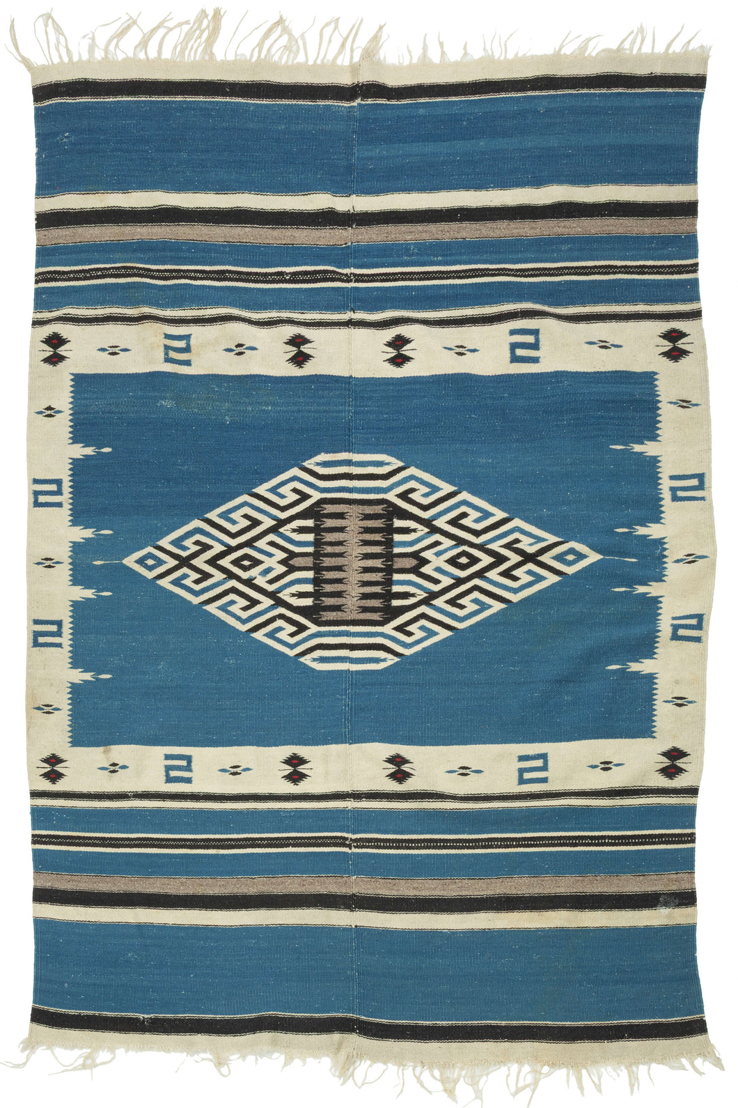 This serape was handwoven in central Mexico during the middle of the 20th century.

A luminous Texcoco serape distinguished by its saturated indigo field and a well articulated central diamond medallion. The stepped, labyrinthine geometry—woven in crisp natural white and deep black creates a powerful visual anchor, while the serrated motifs and butterfly-like accents along the border add nice rhythmic movement.