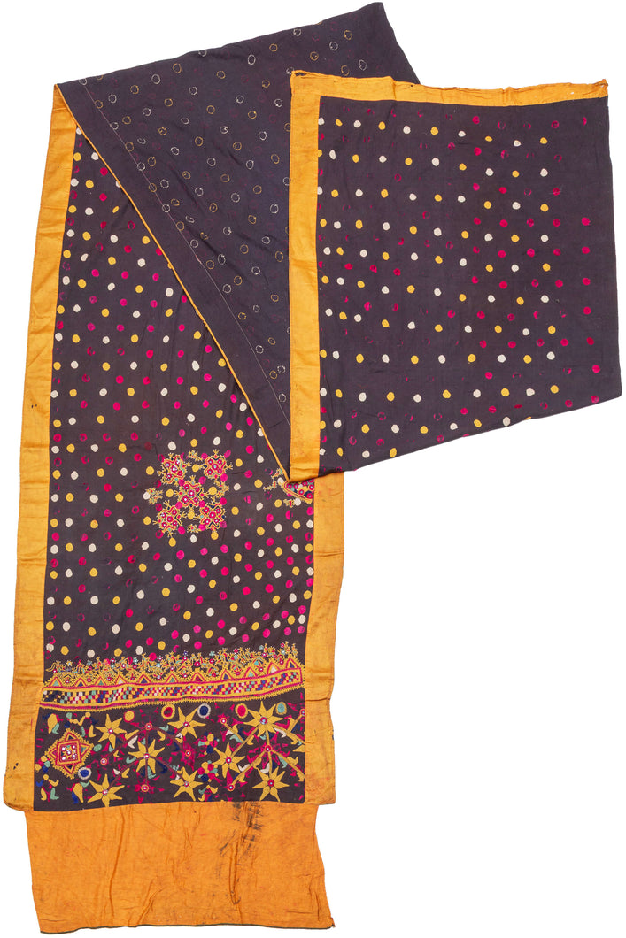 This vibrant ceremonial sari exemplifies the Rabari embroidery tradition of Gujarat. Worked on a lustrous silk ground, the field is covered in hand-embroidered satin-stitch dots in jewel tones of magenta, saffron, and ivory, echoing the region’s famed bandhani aesthetic. The richly decorated end panel features dense floral and geometric embroidery in silk floss threads, highlighted with mirror insets, symbolic of protection and celebration within Rabari culture. Such pieces were created as dowry or ceremoni