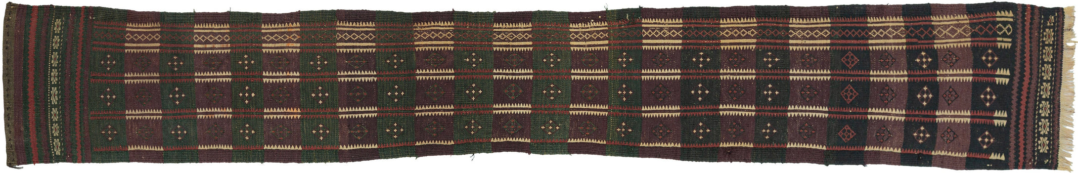 A handsome Baluch trapping with a long, graphic format and a deeply saturated palette of aubergine, forest green, madder, ivory, and dark brown. The design is built from a rhythmic checkerboard of small geometric devices, with serrated ivory bands running vertically through the field and a narrow decorative side border adding balance and movement.