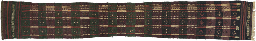 A handsome Baluch trapping with a long, graphic format and a deeply saturated palette of aubergine, forest green, madder, ivory, and dark brown. The design is built from a rhythmic checkerboard of small geometric devices, with serrated ivory bands running vertically through the field and a narrow decorative side border adding balance and movement.