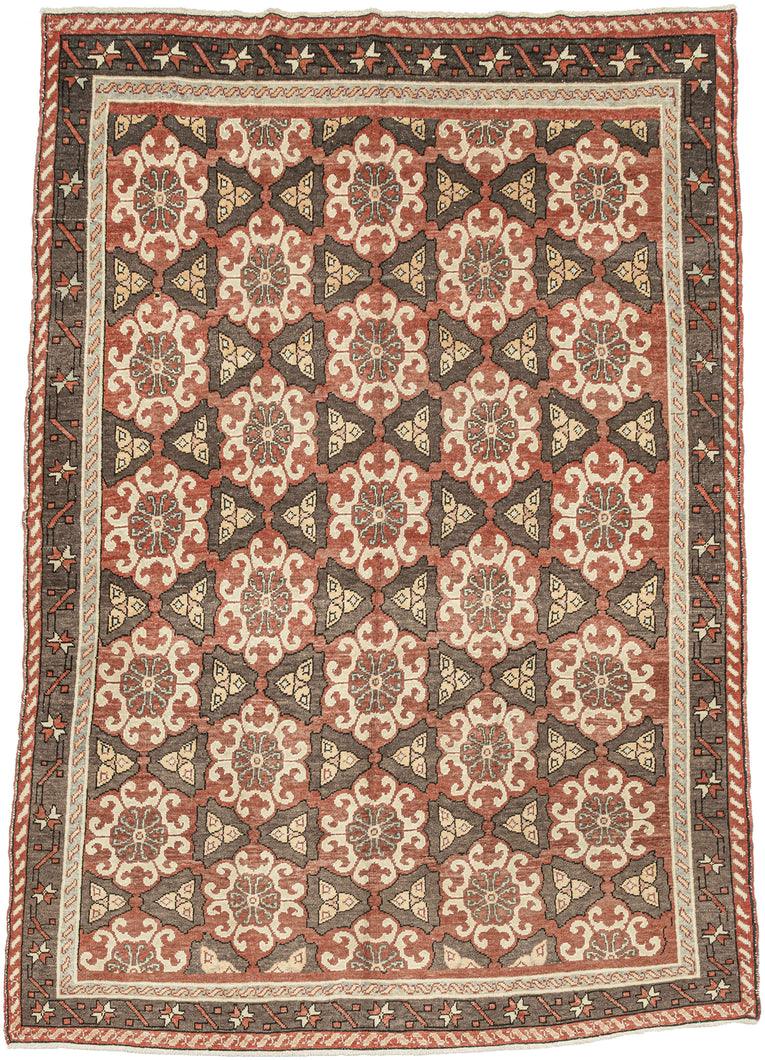 It features a striking allover lattice design with repeating floral rosettes and angular motifs in a balanced palette of earthy terracotta, chocolate brown, ivory, and soft blue. The wide border, decorated with stylized stars and angular vine elements, frames the field beautifully, adding depth and structure to the pattern. The bold yet harmonious composition and soft tones exemplify the sophisticated village weaving traditions of the region. KONYA