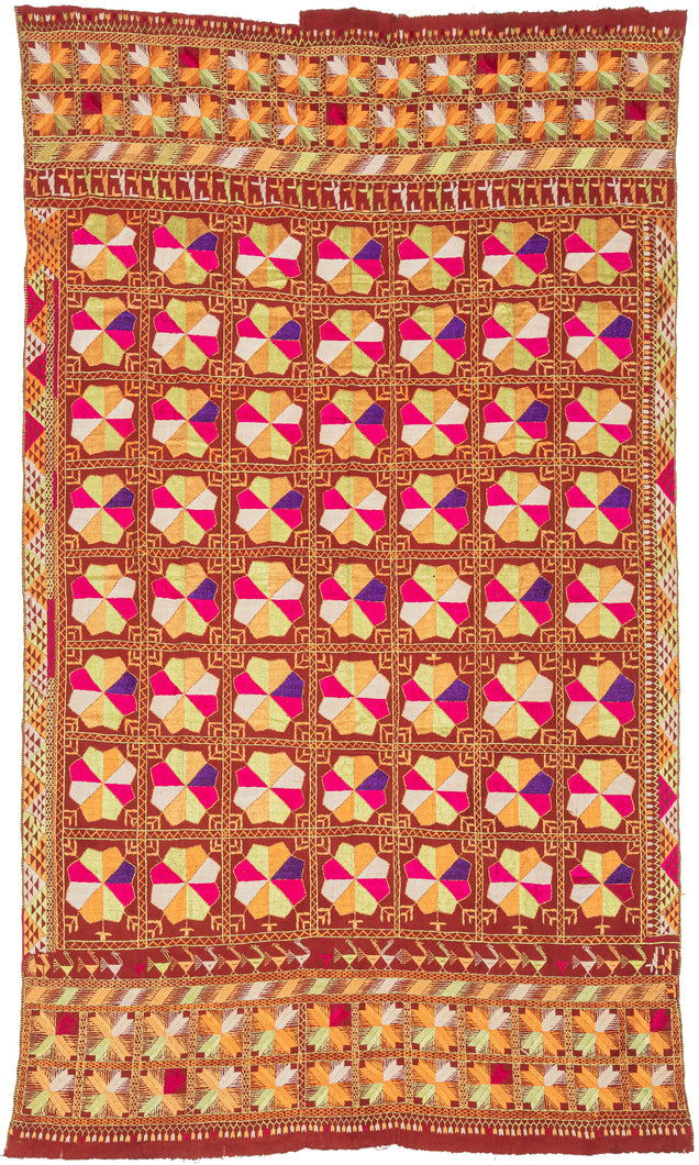 Phulkari is a traditional folk embroidery style from the Punjab region, which spans both India and Pakistan. It is composed of colorful silken thread atop rough cotton cloth. This Phulkari was embroidered in silk floss on multiple red cotton strips and features a striking composition of kaleidoscopic floral medallions arranged in a dense grid. Finished with skirt borders of interlocking motifs, including zoomorphic bird-like figures on one end.  Highly contrasting tones of fuchsia, saffron, pistac