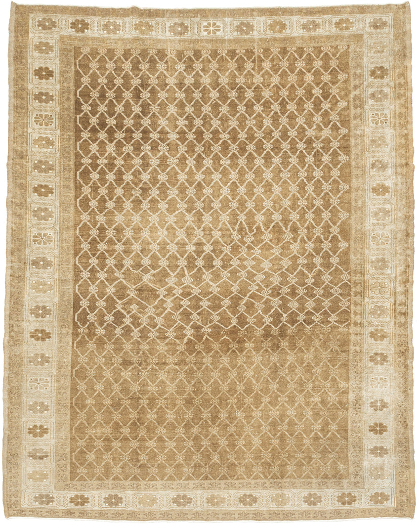 KURD Its warm camel field is animated by a playfully wonky interlocking lattice and framed by a border of larger floral medallions in soft ivory and beige. The lattice has the feel of a bent and distorted chain link fence. The delightful irregularity in the design has an endearing quality that speaks to its handmade nature and gives the piece a unique, almost whimsical character. The washed out neutral palette and subtle abrash create a natural warmth, making it a versatile choice for both traditional