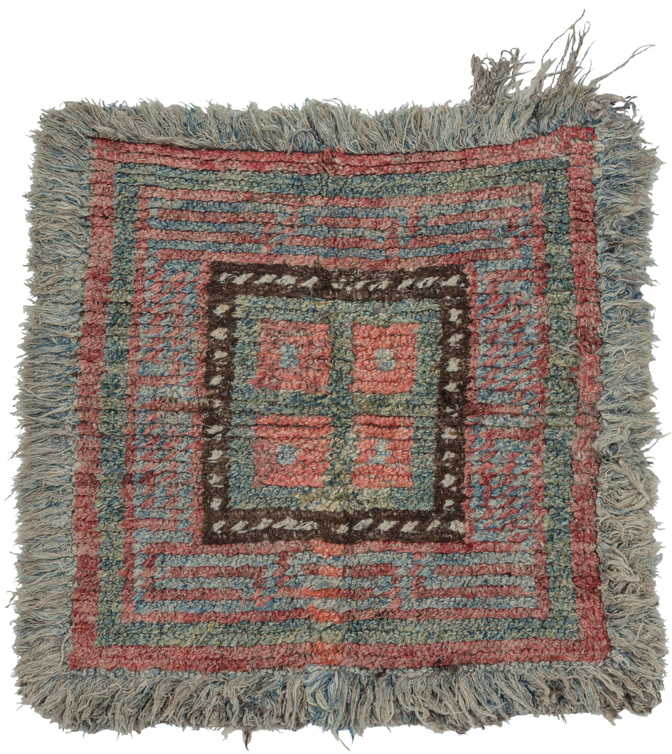 A compact Tibetan Wangden woven in the Wangden Valley of eastern Tibet, organized around a bold nested square composition. Stepped meanders radiate outward from a central panel, creating a rhythmic, architectural framework that balances symmetry with subtle irregularity. The palette of muted coral, slate blue, and mineral green is anchored by a dark brown inner border punctuated with small ivory accents.

Woven in hand-spun wool with a dense, springy pile, the piece retains its original long fringe and disp