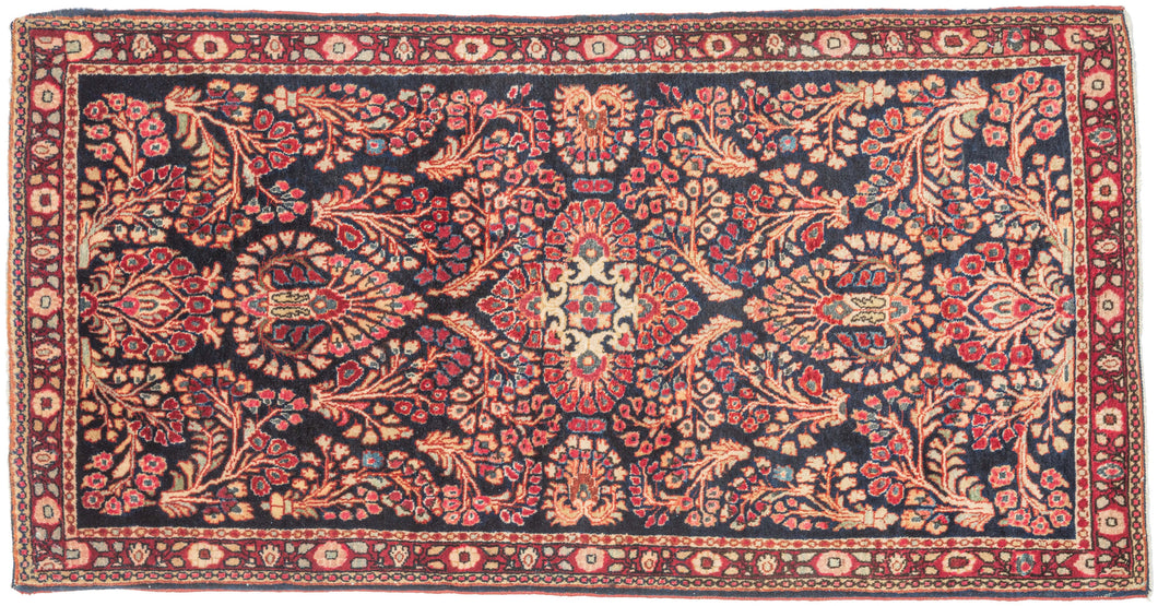 This finely woven Sarouk exemplifies the lush floral language that made the region’s carpets among the most sought-after of 1920s. Set against a deep midnight-blue ground, an intricate lattice of scrolling vines, palmettes, and rosettes unfolds with remarkable density and clarity, anchored by a subtle central medallion that gives structure to the otherwise allover composition.