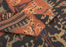 An Indonesian cotton ikat from Sumba with contrasting horizontal bands of deep indigo and warm rust. Stylized animal and ancestral motifs emerge rhythmically across the dark ground, their forms softened by the characteristic feathered edges of the resist-dye technique.