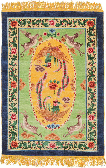 This silk rug was handwoven during the 3rd quarter of the 20th century in Tianjin, China.It features a central scene of two mythological fenghuangs surrounding a red and pink peony on a yellow ground. The yellow oval is flanked by four prancing stags on a seafoam green ground. The whole is framed by a border of blossoming red and pink peonies on green vines and finished a thick block of navy around the perimeter.