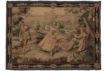 Antique  French Aubusson tapestry depicting a bucolic scene of a "coquette" and two potential suitors. At the center of the scene, a woman lifts her skirts to reveal an ankle towards a man propped up against a tree, playing a lute. A second man passes by and both him and the woman take notice of another. A house is visible in the background, as is a body of water. A very dainty meander of ribbon and flowers frames the scene as the border. 