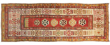 This Kazak Runner features a thin field of polygons on a red ground with arrows near a small green section at the top giving the pattern subtle directionality. The polygons are filled with protection symbols and slightly shift in scale unintentionally. It is framed by a very wide and relatively bright ivory main border with large-scale geometric devices in red, yellow, green, and icy blue.