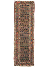 This Antique Kurdish Bidjar Runner features a field filled with offset rows of plump, polychrome botehs on a dark navy ground. The field is framed by a main border of scrolling vine work with alternating blossoms in attractive shades of red, blue, and yellow against a soft brown ground. It is flanked by two minor borders with a variation of the same pattern but less precise, on a smaller scale and in a perfectly contrasting ivory ground.