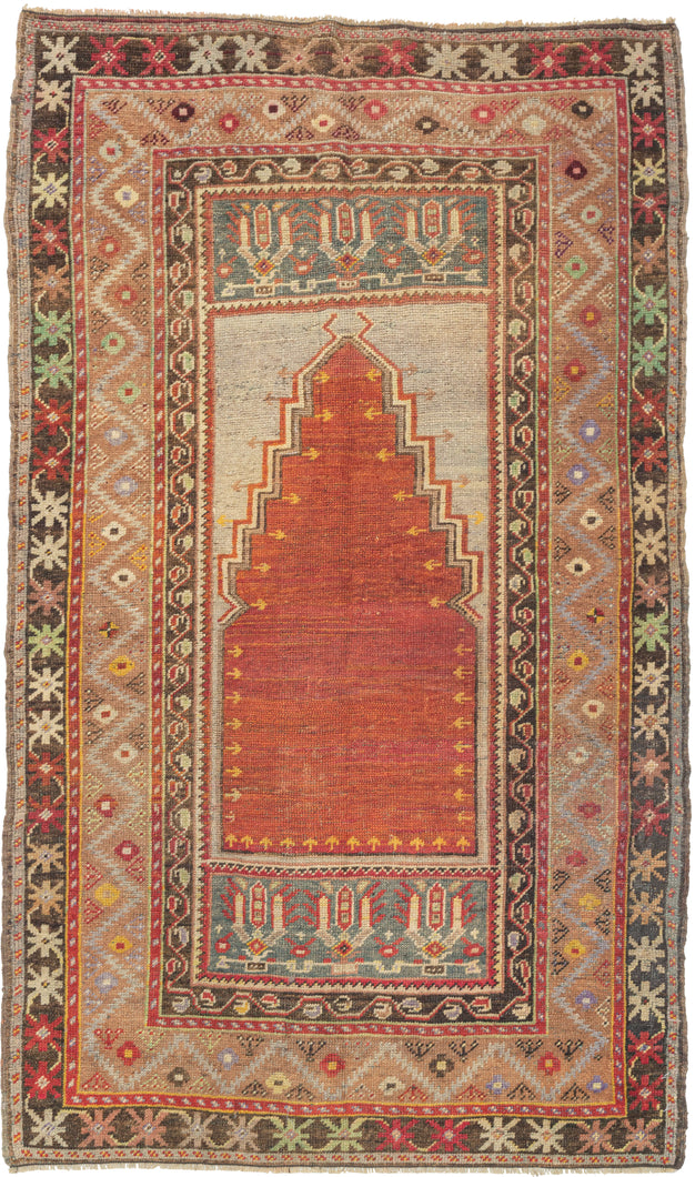 Antique Turkish prayer rug featuring the classic long and narrow latch-hooked Mihrab associated with the town of Nigde between Yahyali and Konya in central Anatolia. The main field is composed of the rich orangey-red mihrab on a silvery ground of faded fuchsine dyes and flanked by two cartouches each with rows of three stylized blossoms. With a main border featuring a soft zigzag meandering around olive-like cintamani symbols on a caramel ground.