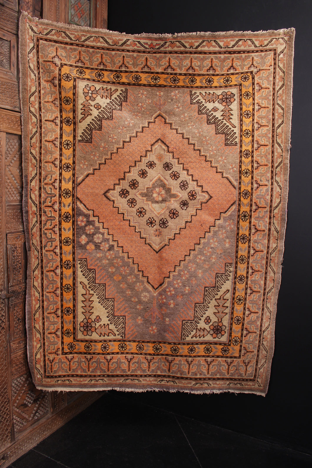 Khotan rug handwoven second quarter of 20th century in Northwest China. Orange-pink peach tones and soft grey browns. Slightly off center medallion framed by small flowers 