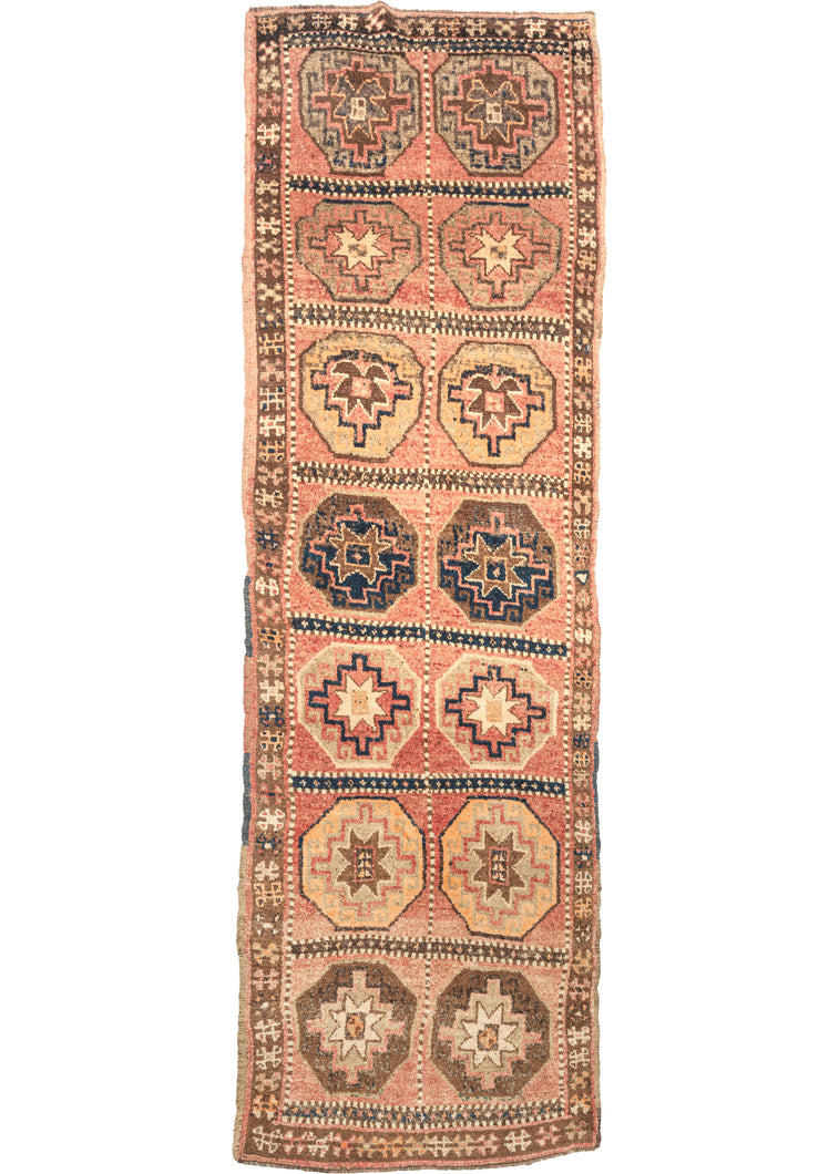 This Mid Century Kars Runner features features a large grid full of fun and wonky memling guls in reds, browns, yellows, and navy on the faded coral ground.  The field is framed by a simple thin brown border and the edges have been finished with multiple selvages.